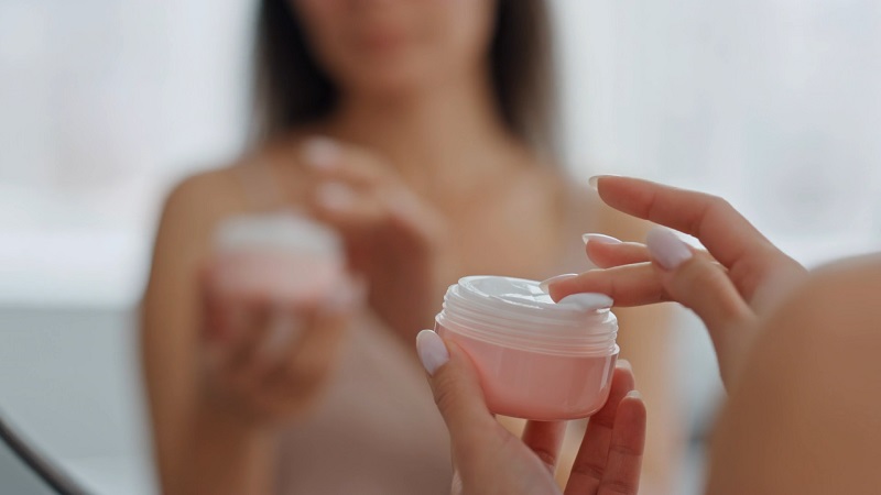 Woman opening a jar of moisturizer that may contain ingredients causing a burning sensation on sensitive skin