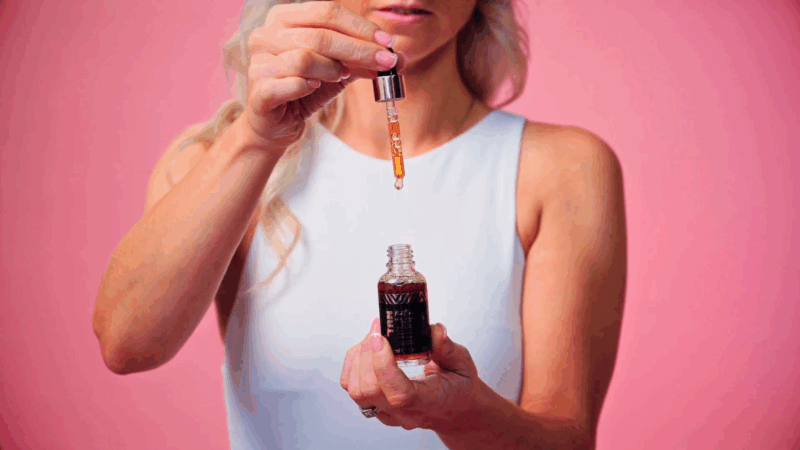 A woman holding a dropper with self-tanner over a bottle