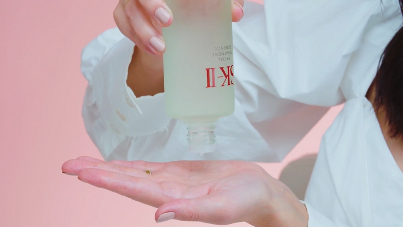 A person pouring facial essence from a bottle into their hand