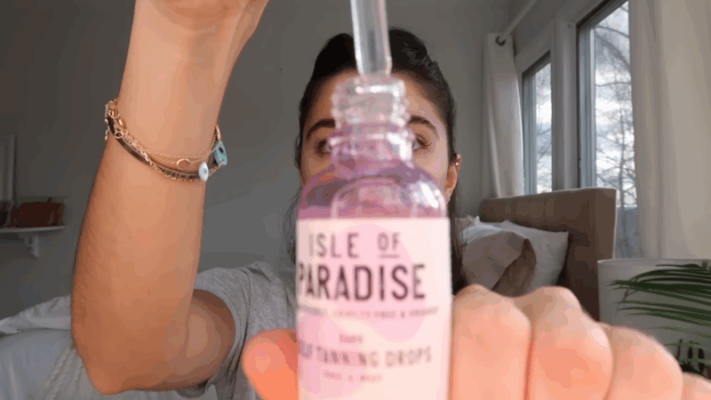 A person holding a bottle of Isle of Paradise Face Self-Tanning Glow Drops with the dropper in use