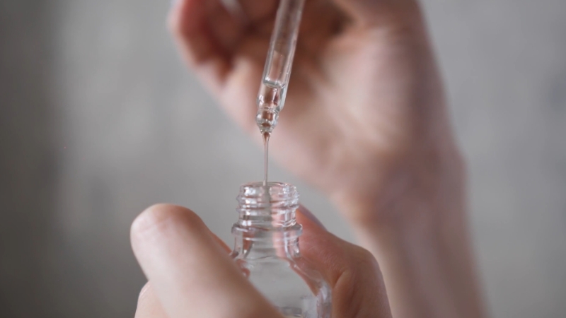 A person using a dropper to apply serum from a small glass bottle