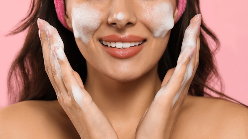 A woman smiling while applying foam cleanser to her face