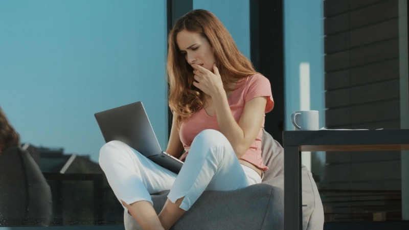 A woman sits outside with a laptop, looking concerned while reading skincare product information online