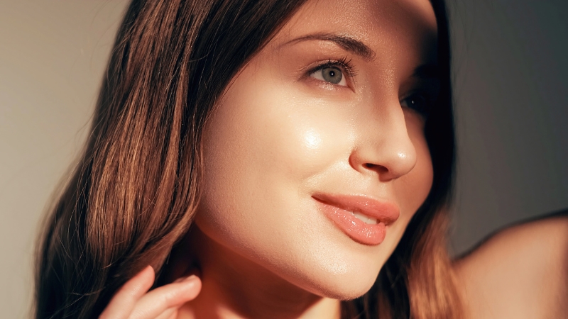 A woman with smooth, radiant skin stands in soft light, showing the effect of glow-boosting skincare