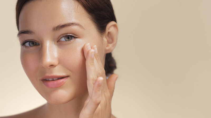 Woman with glowing skin applying primer to her cheek, showing a natural look using only primer and setting spray