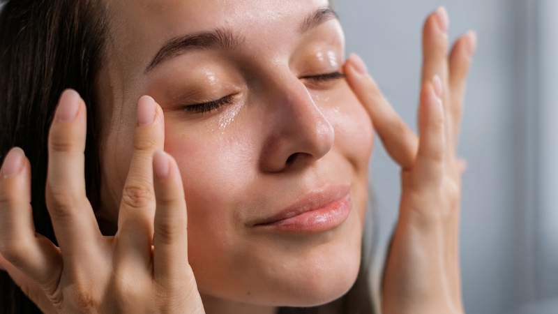 A woman gently presses primer into her skin, showing a fresh, glowing look achieved without foundation