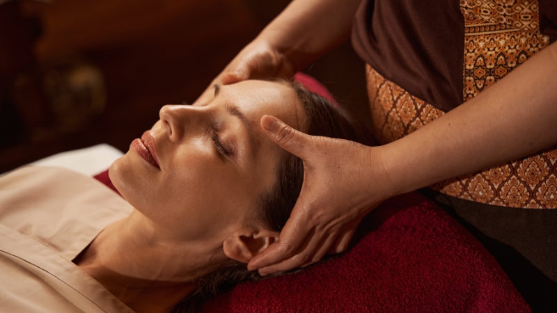 A spa therapist gently massages a woman's head to create a relaxing experience for spa clients
