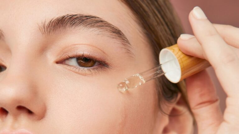 A woman applies serum with a dropper to her cheek, showing how facial oils for mature skin boost hydration and radiance