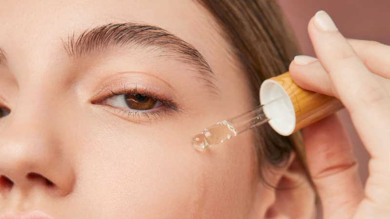A woman applies serum with a dropper to her cheek, showing how facial oils for mature skin boost hydration and radiance