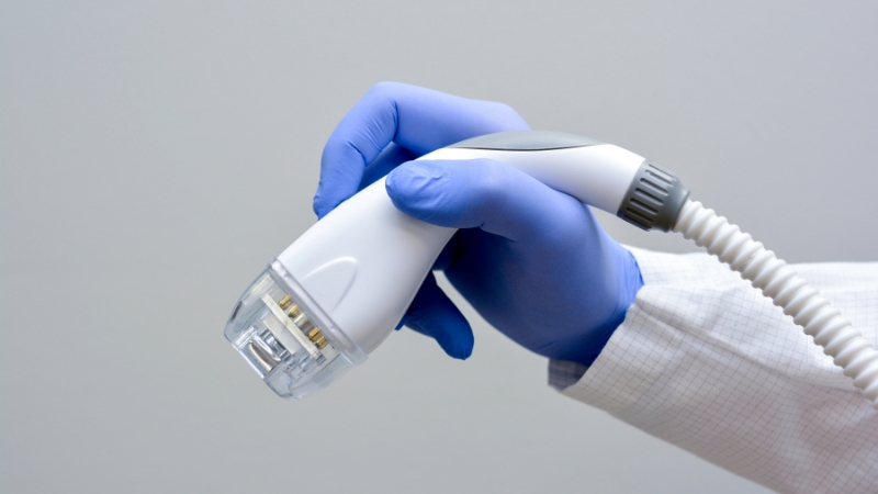 A gloved hand holds a radiofrequency skin tightening device used in noninvasive cosmetic treatments