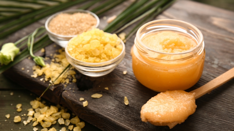 A jar of DIY turmeric face scrub with small bowls of sugar and sea salt on a wooden board