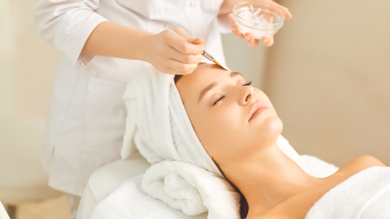 A woman receives a chemical peel treatment applied with a brush during a spa session