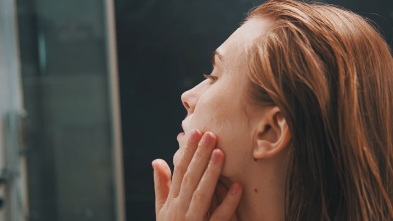 A woman gently applies skincare to her face as part of a treatment aftercare routine