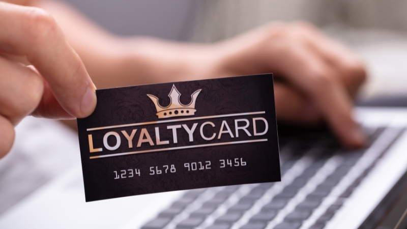 A hand holding a loyalty card in front of a laptop