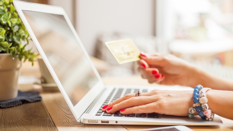 A woman using a laptop and holding a bank card, showing the role of privacy and trust in beauty e-commerce