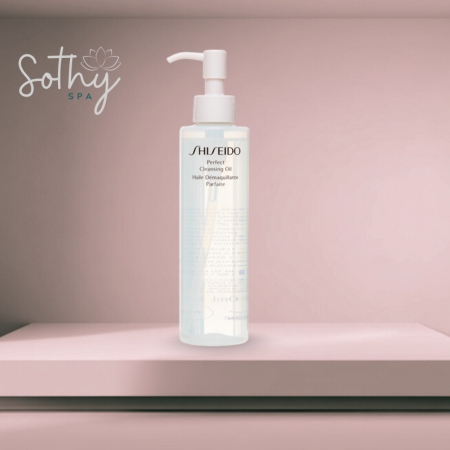 Clear bottle of Shiseido Perfect Cleansing Oil with a white pump, placed on a pink spa-themed shelf background
