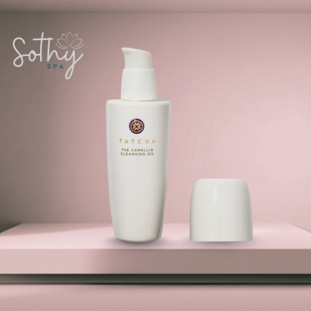 Bottle of Tatcha The Camellia Cleansing Oil with pump and cap placed beside it, displayed against a soft pink background with a spa logo
