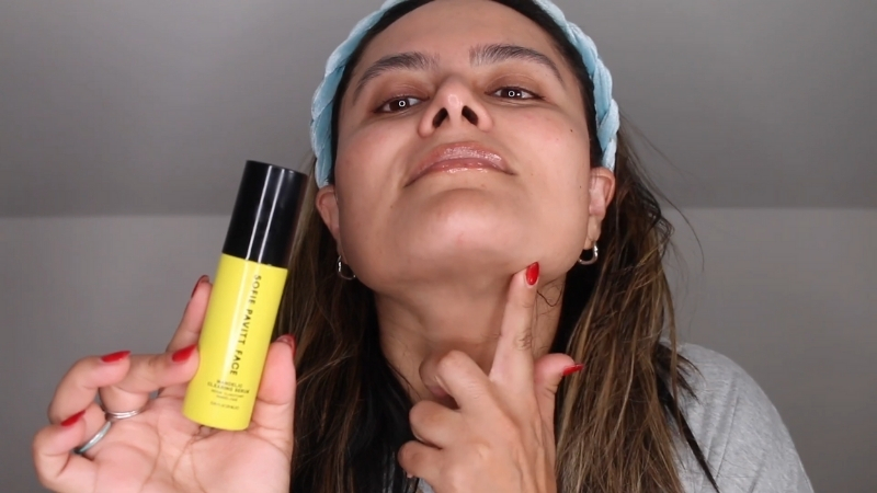 A person applies Sofie Pavitt Face Mandelic Clearing Serum while holding the yellow bottle close to the face