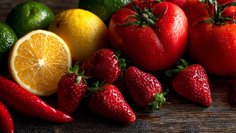 Fresh fruits rich in vitamin C, including oranges, strawberries, tomatoes, and chili peppers on a wooden table